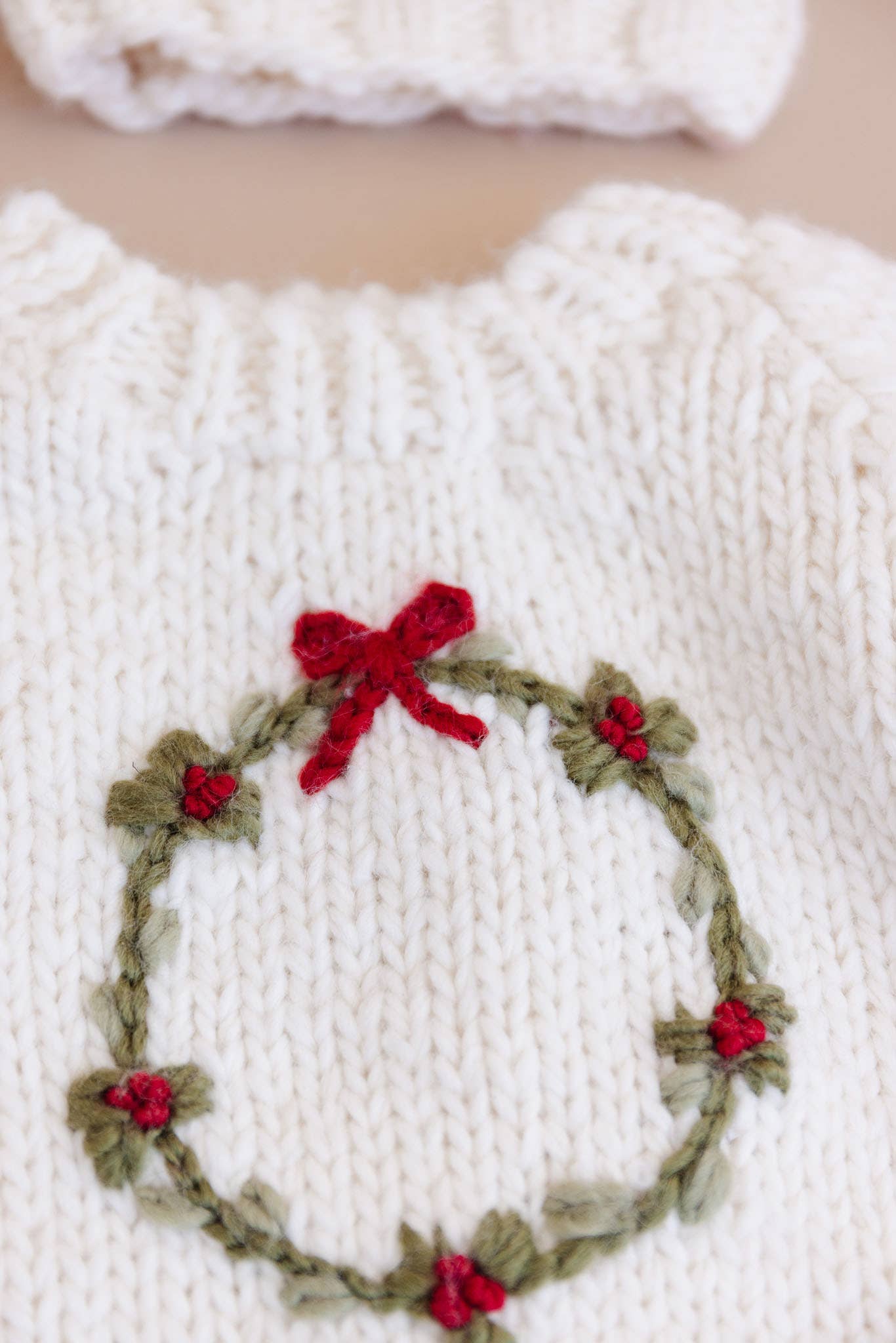 Close-up of the embroidered wreath, red berries and bow on the Wreath Sweater